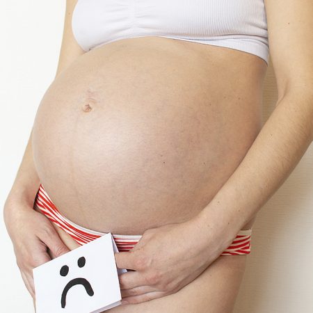 mulher gravida segurando uma plaquinha de cara triste em volta da barriga gravida