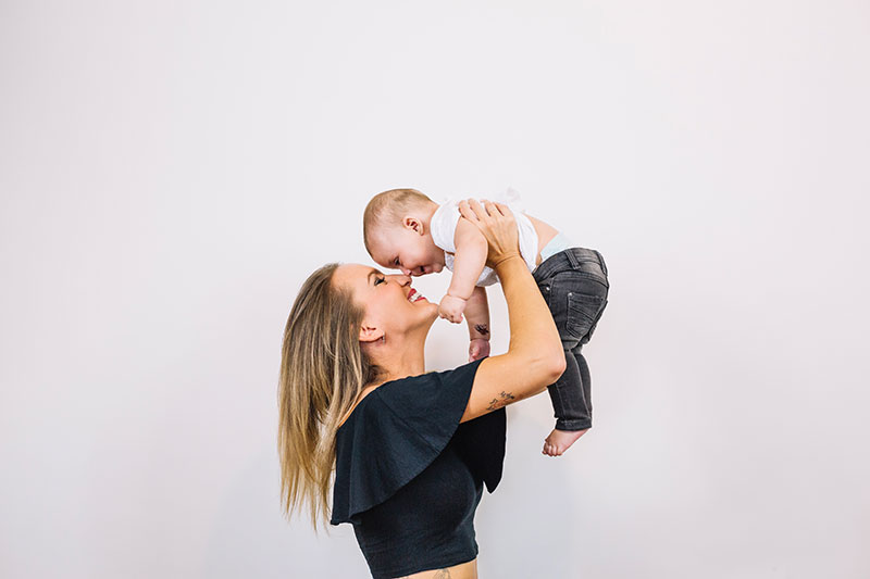 Mãe levantando seu filho para o ar em um fundo cinza