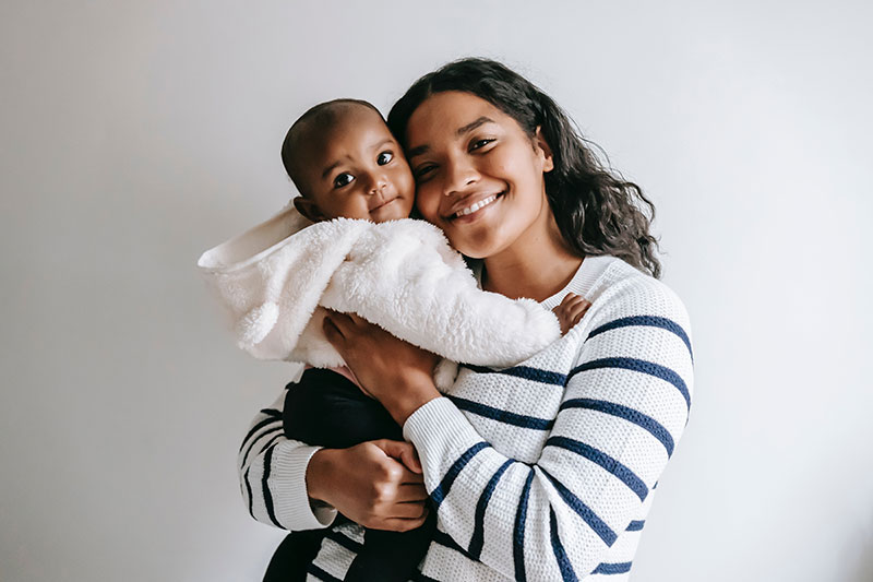 Uma mulher negra segurando seu filho sorrindo para a câmera para ilustrar o benefício maternidade