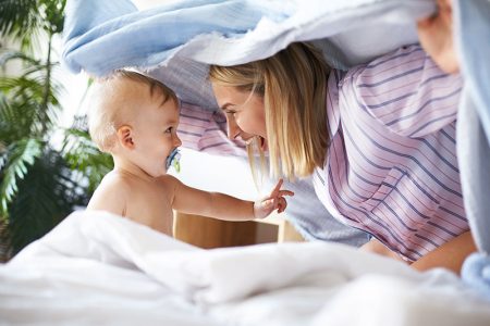 Mãe fazendo surpresa para o filho com uma coberta para ilustrar o benefício maternidade e o salario maternidade